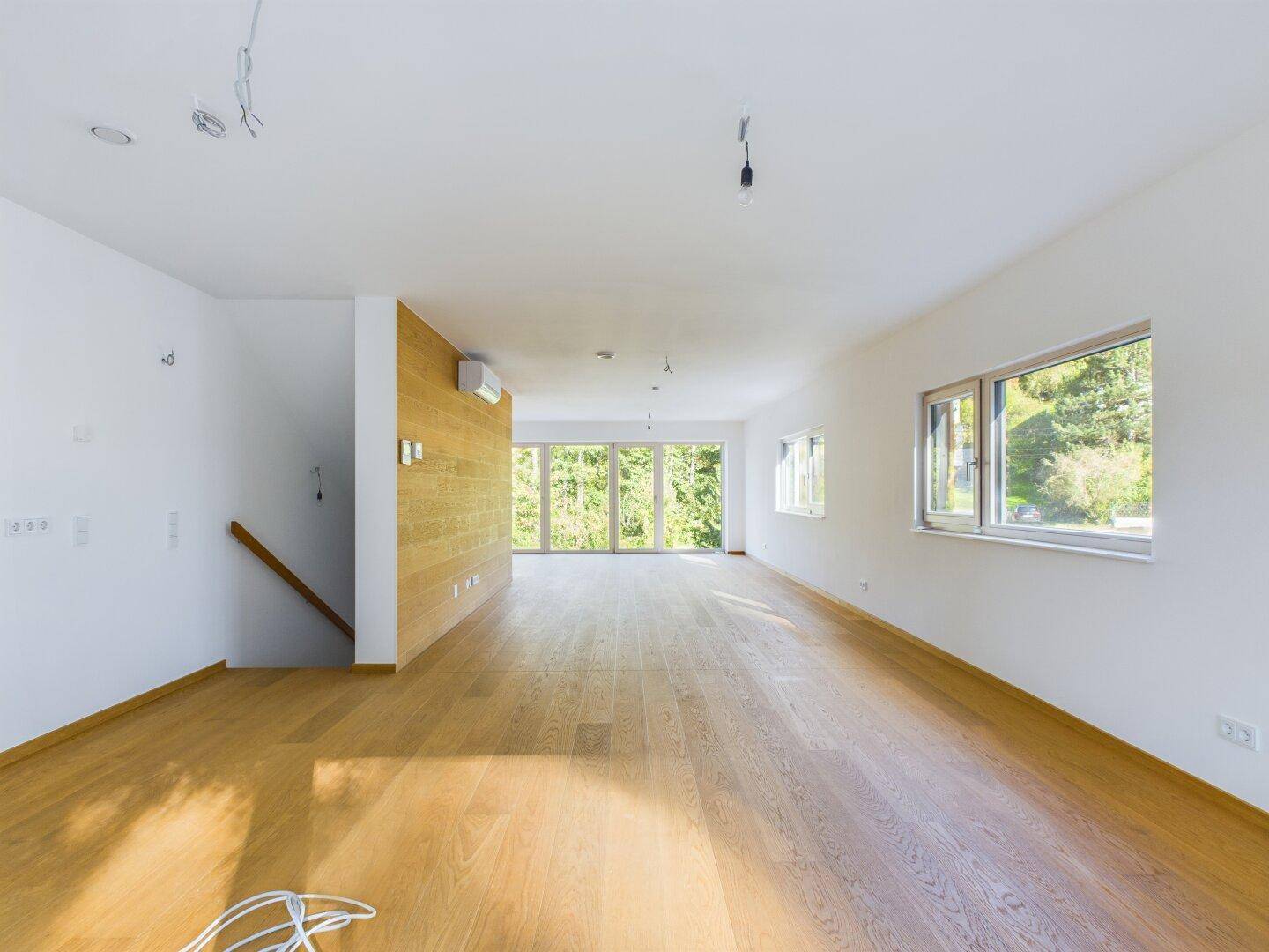 Lichtdurchfluteter Wohnbereich mit Holzboden und einer Holzwand, die den Raum strukturiert.