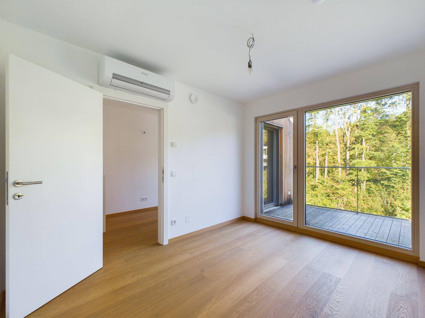 Schlafzimmer mit Holzboden, Klimaanlage und Zugang zu einem Balkon mit Waldblick.