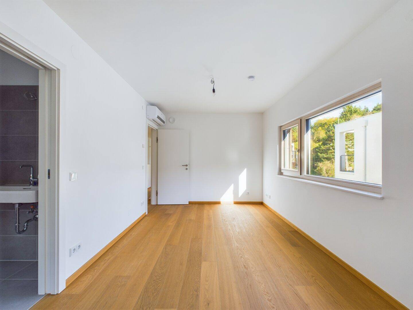 Geräumiges Schlafzimmer mit Holzboden, Klimaanlage und Blick auf die umliegende Natur.