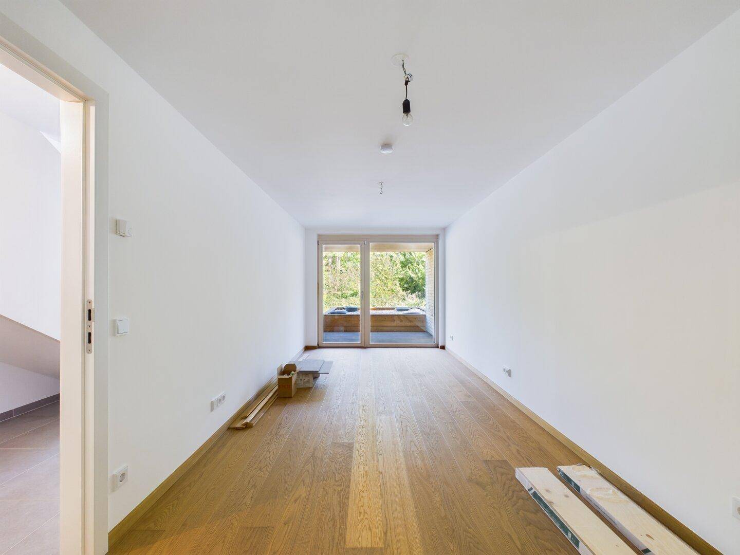 Leeres Schlafzimmer mit Holzboden und Zugang zu einem Balkon mit Blick ins Grüne.