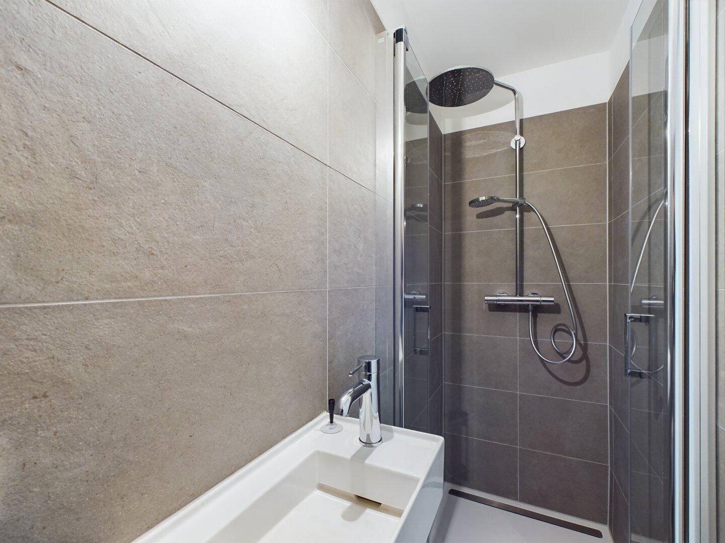 Modernes Duschbad mit bodengleicher Dusche, Regenbrause und minimalistischem Waschbecken.