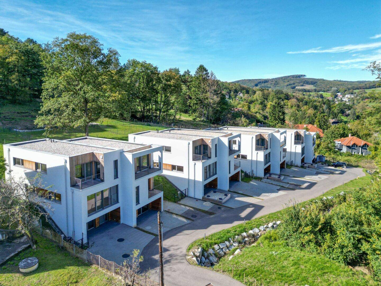 Reihe moderner Reihenhäuser mit weißer Fassade und Holzdetails in einer grünen Hügellandschaft.