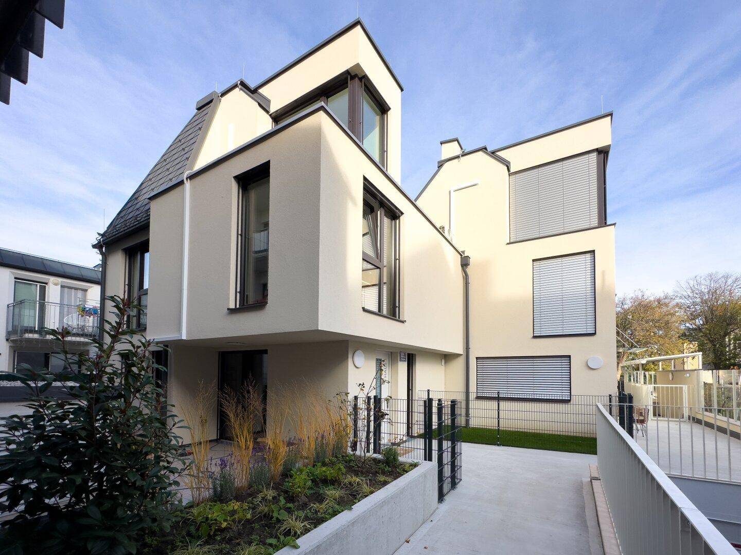 Seitenansicht des Neubaus mit moderner Architektur, großen Fenstern und gepflegter Bepflanzung im Außenbereich.