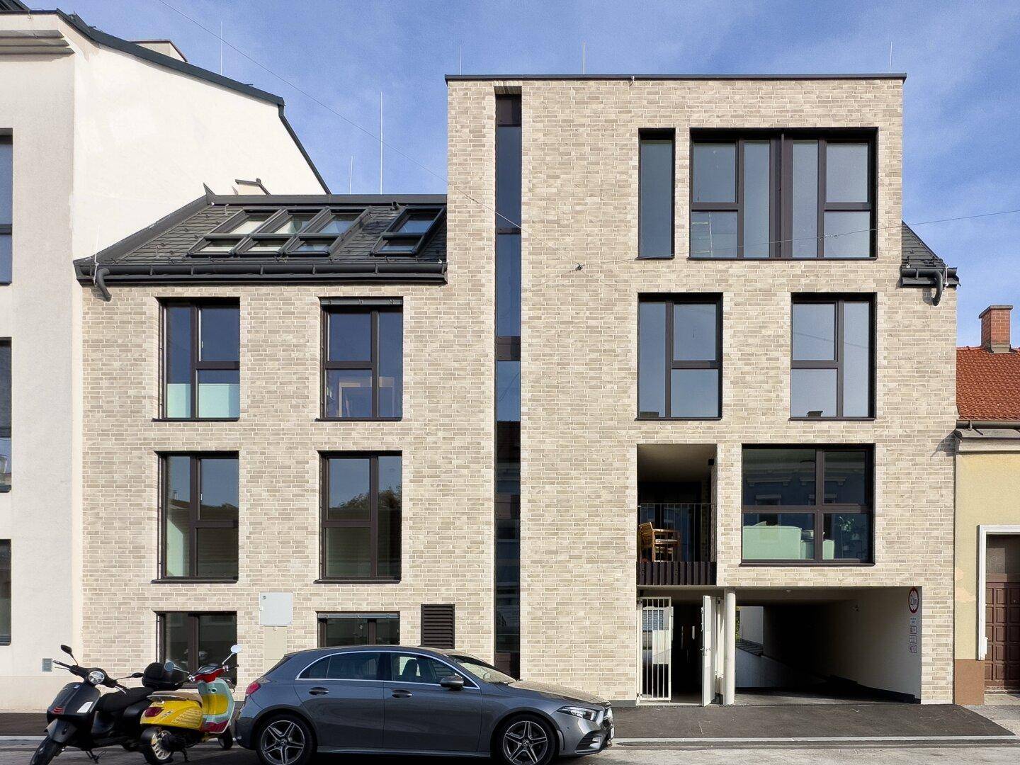Moderne Wohngebäude-Fassade mit heller Ziegelverkleidung, großen Fenstern und Balkonen.