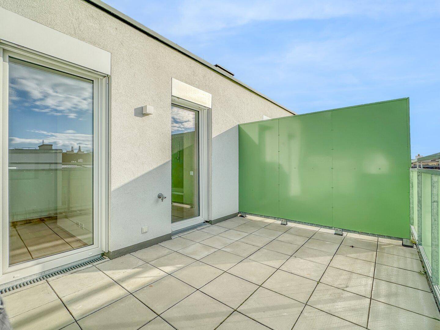 Große, sonnige Terrasse mit Fliesenboden und Blick auf die städtische Umgebung.