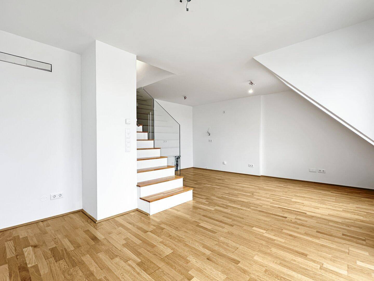 Geräumiger Wohnbereich mit moderner Treppe und Holzparkettboden in einem Neubau-Apartment.