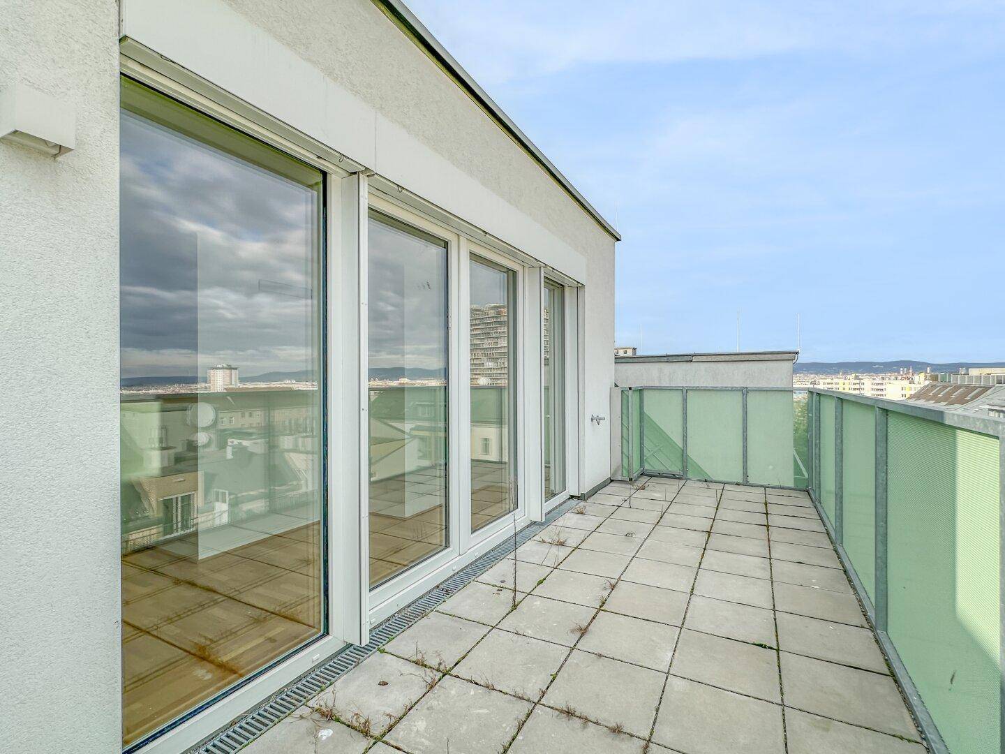 Geräumige Terrasse mit Fliesenboden und großen Glasfronten zum hellen Innenbereich.
