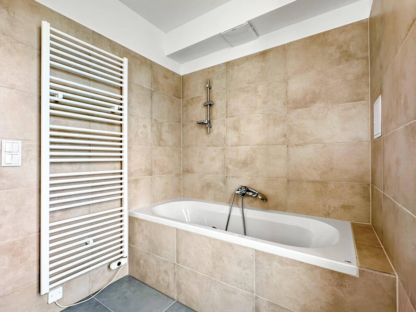 Badezimmer mit Badewanne, beigefarbenen Fliesen und beheiztem Handtuchhalter.