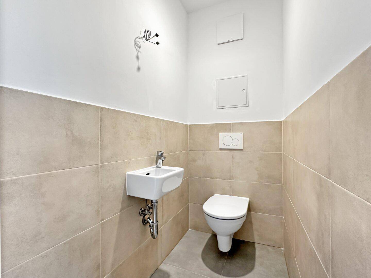 Separates Gäste-WC mit Wand-WC, kleinem Waschbecken und modernen Fliesen.