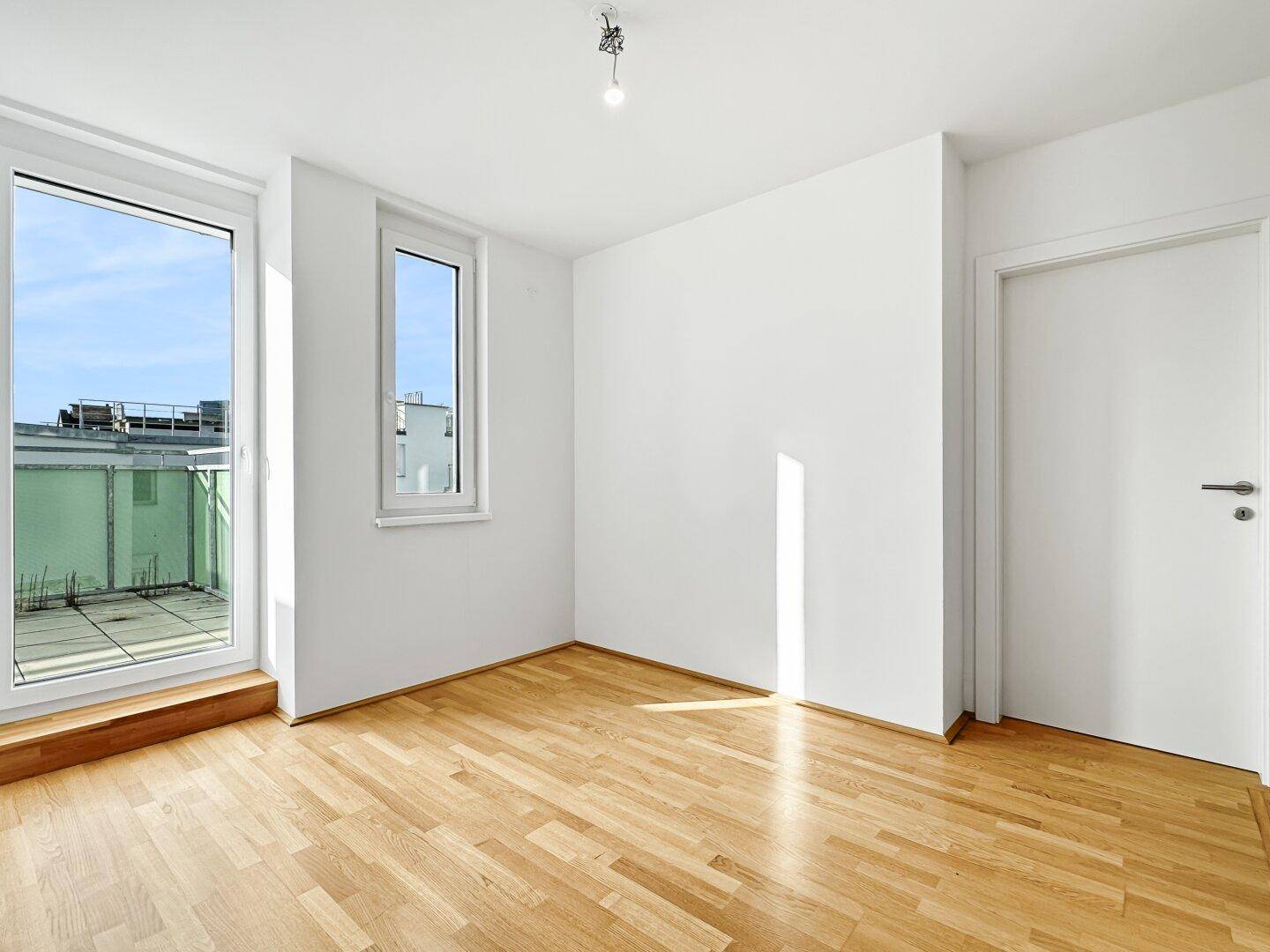 Helles Schlafzimmer mit Holzparkettboden und direktem Zugang zu einer sonnigen Terrasse.