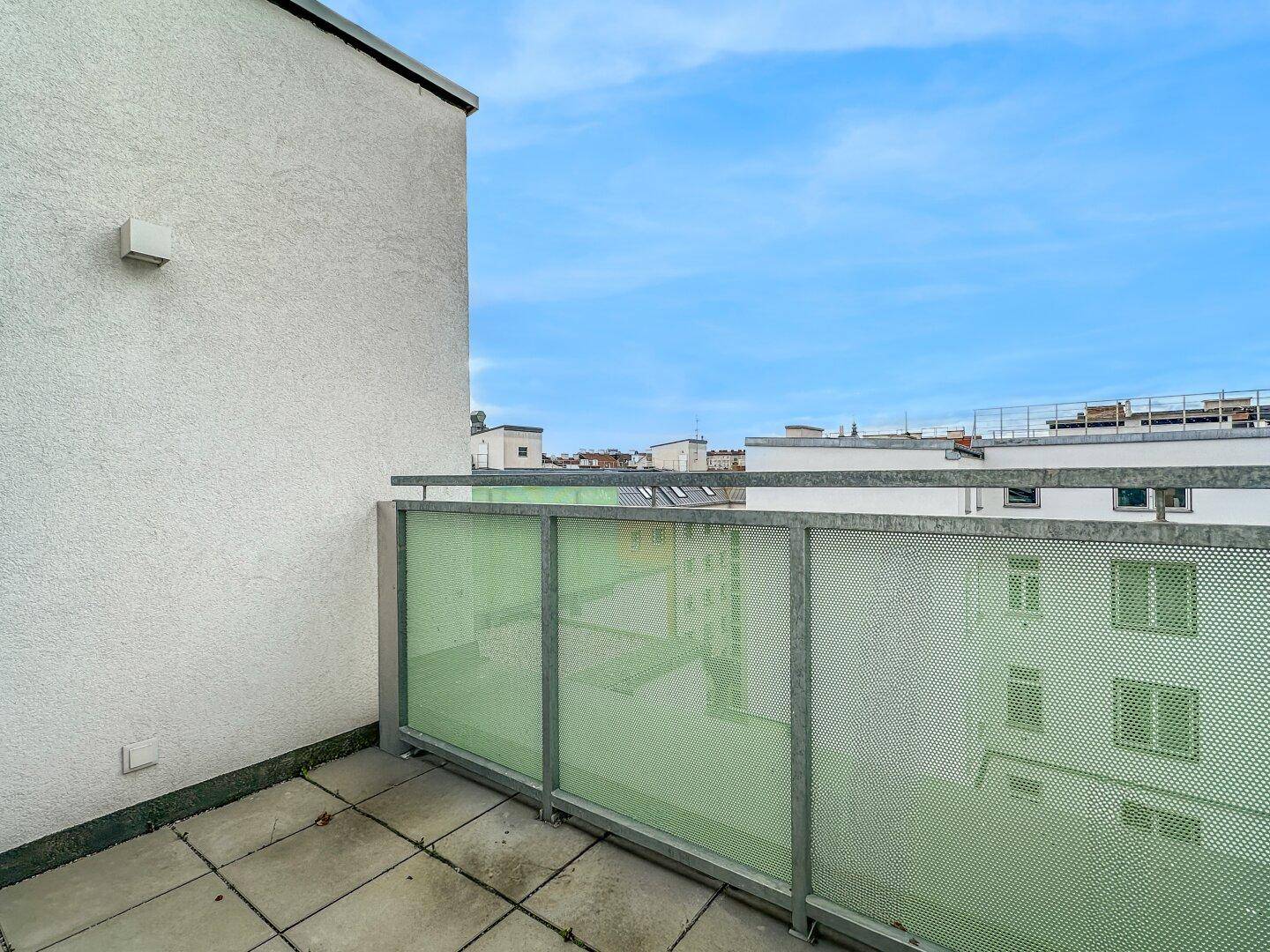 Balkon mit moderner Lochblech-Brüstung und Fliesenboden, bietet einen weiten Stadtblick.