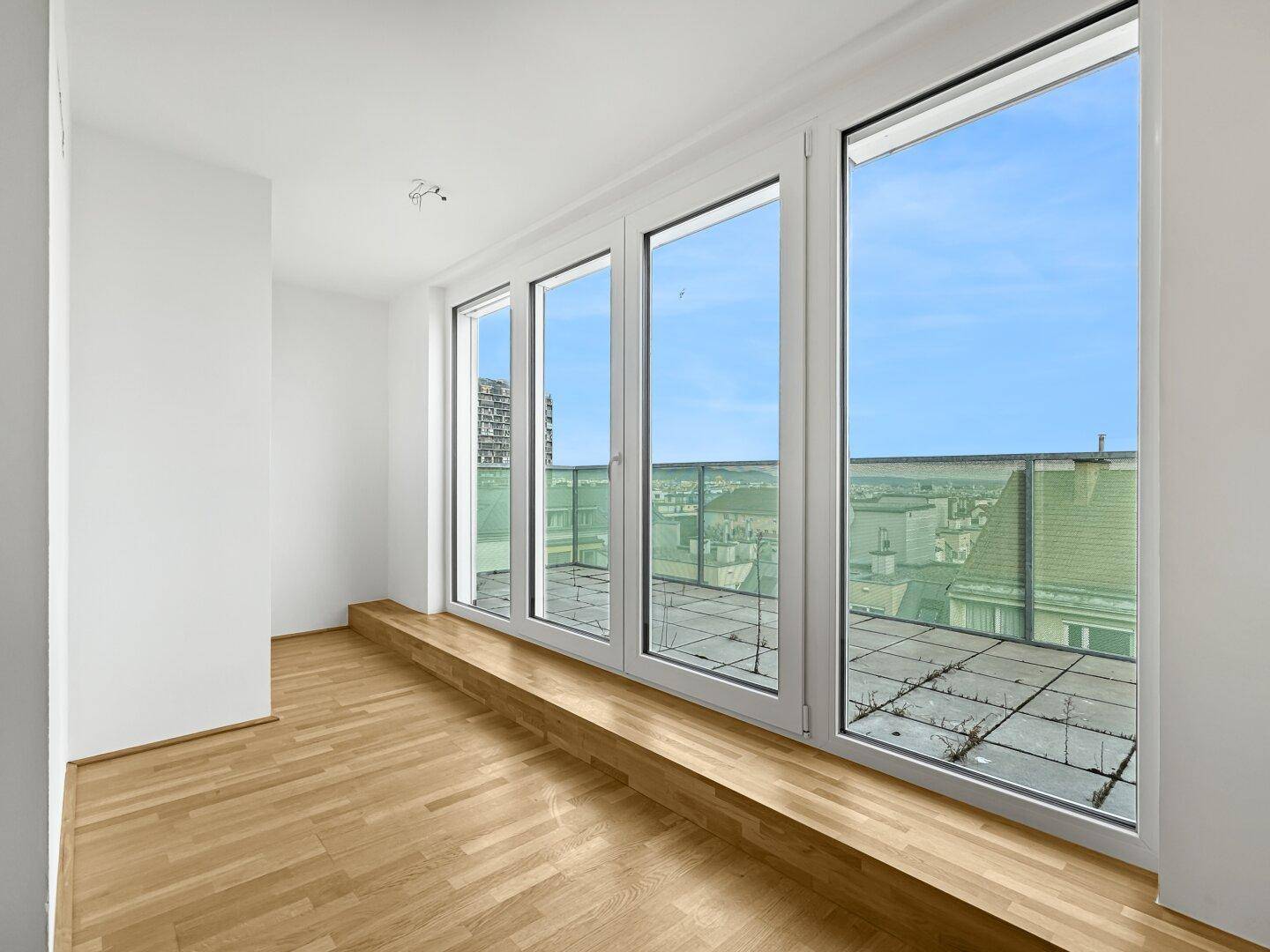 Lichtdurchfluteter Raum mit großen Fenstern, Holzparkett und weitem Stadtblick.