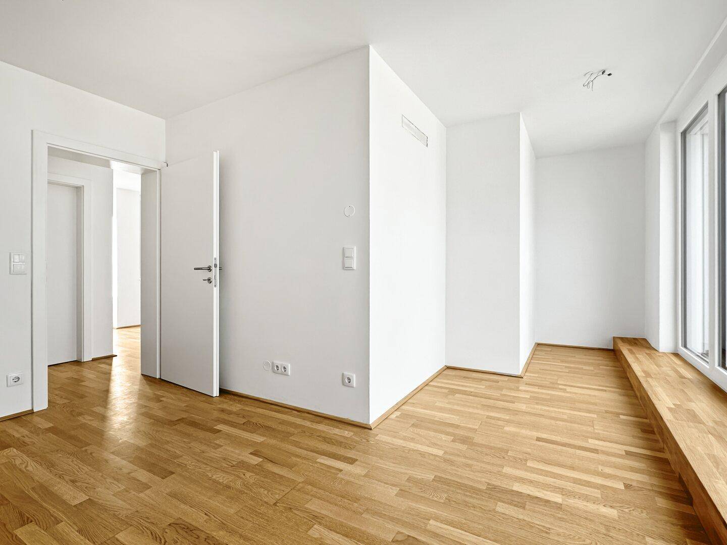Heller Wohnbereich mit Holzparkettboden und Zugang zu weiteren Räumen der Wohnung.