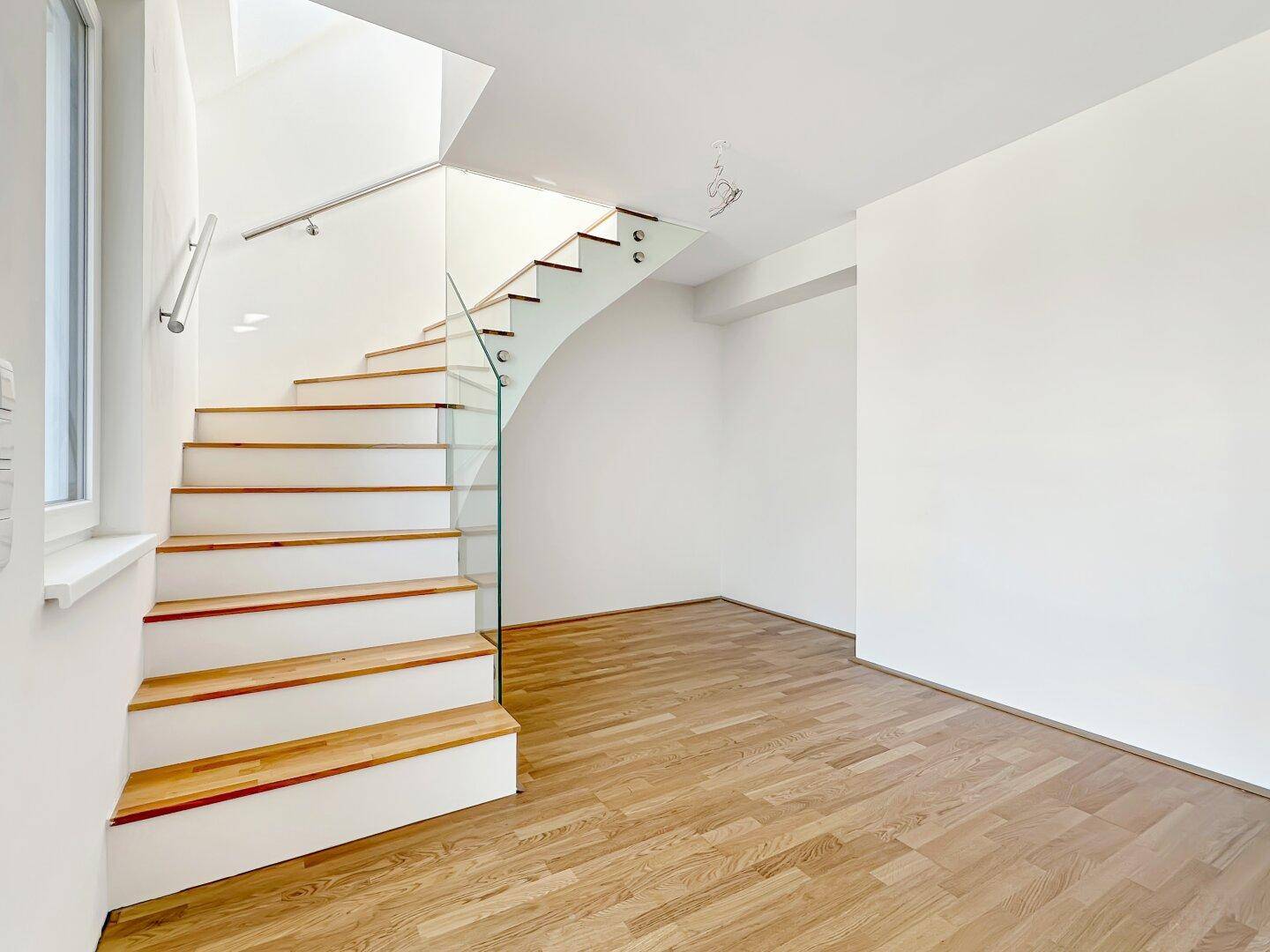 Heller Flurbereich mit moderner Treppe aus Holz und Glasgeländer.