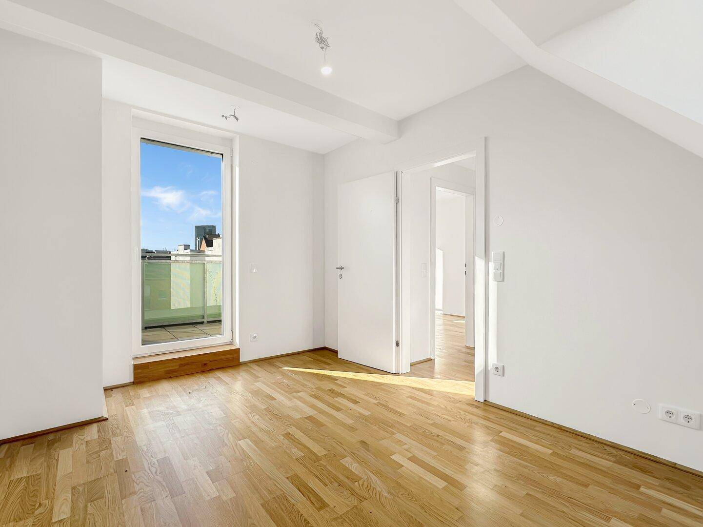 Geräumiges Schlafzimmer mit Parkettboden, Zugang zur Terrasse und schrägen Decken.