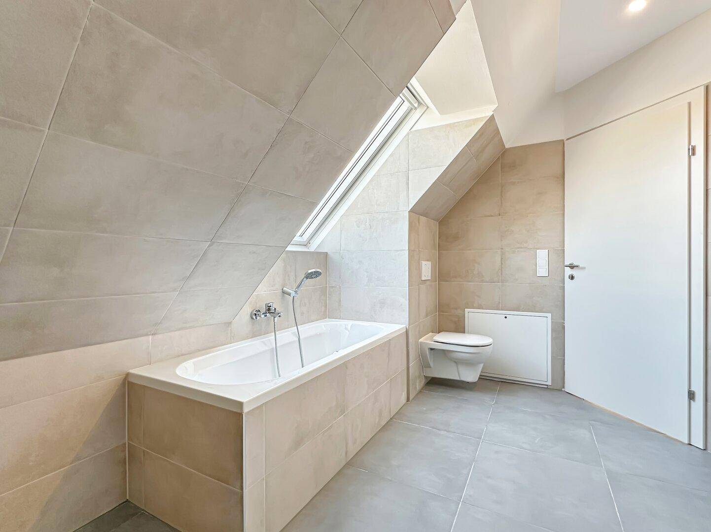 Helles Badezimmer mit Badewanne, wandhängendem WC und Dachfenster für natürliches Licht.