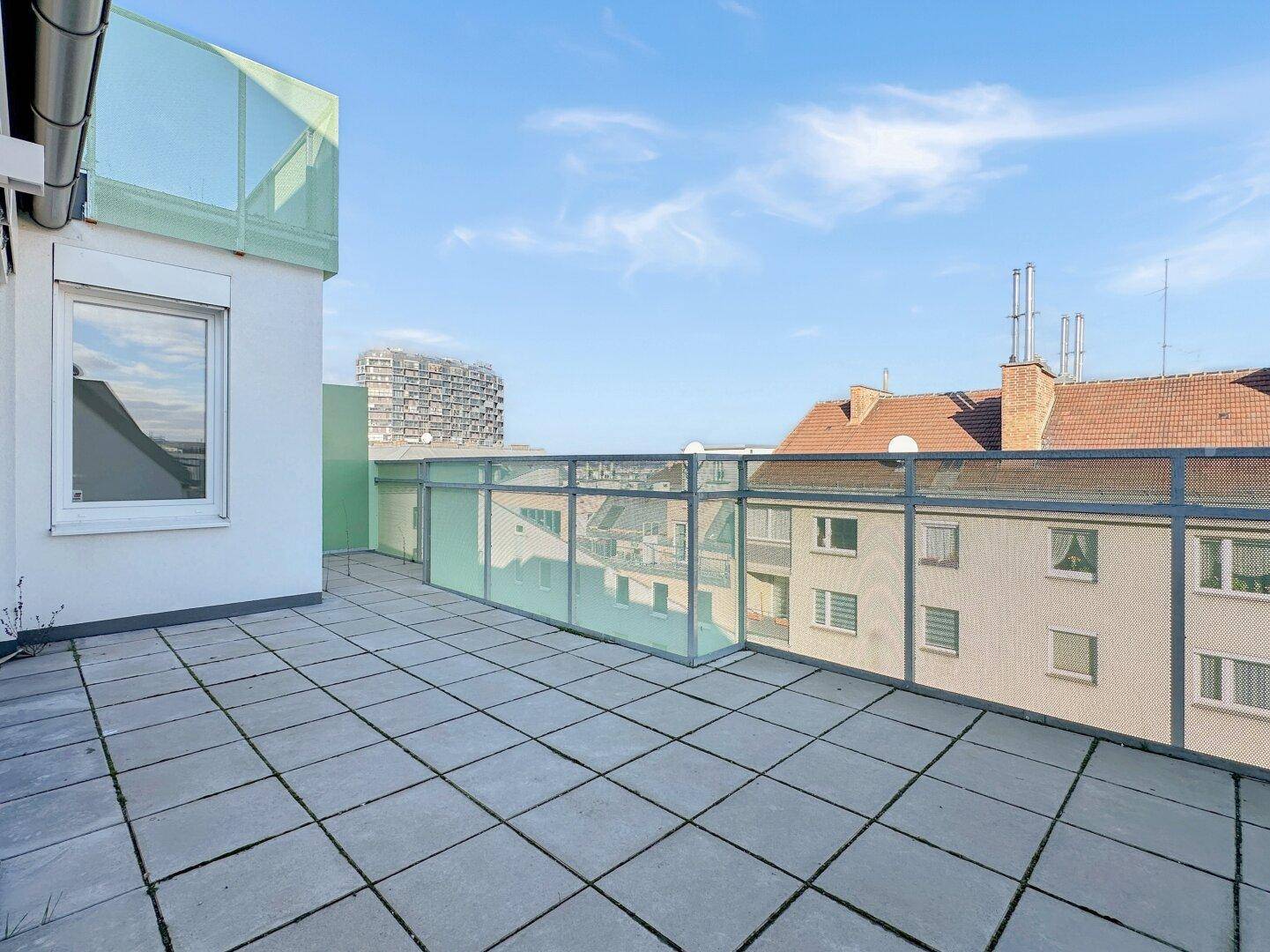 Geräumige Dachterrasse mit Fliesenboden und Blick auf die umliegenden Gebäude.