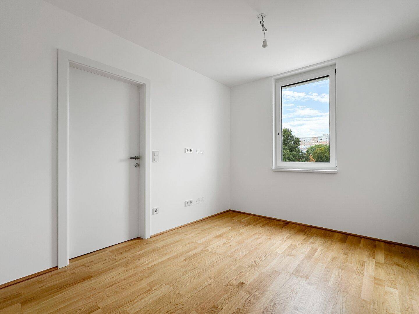 Helles, leeres Zimmer mit Holzboden und weißer Tür, bereit zur individuellen Gestaltung.