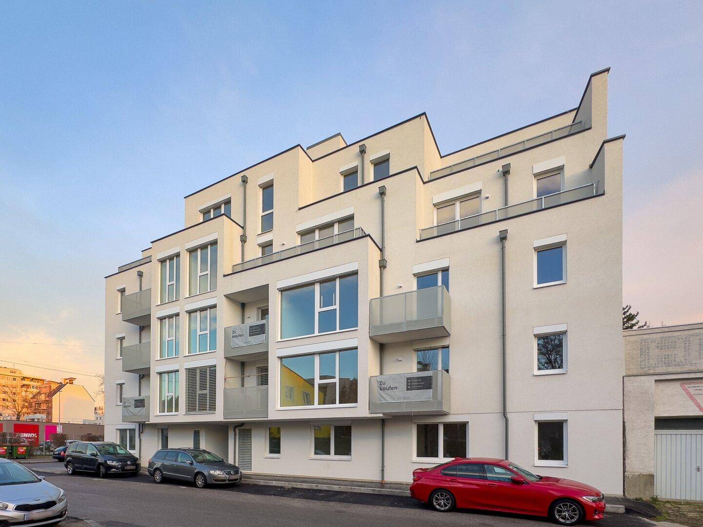 Zeitgenössisches Wohngebäude mit heller Fassade, gestuften Balkonen und großen Glasflächen unter blauem Himmel.