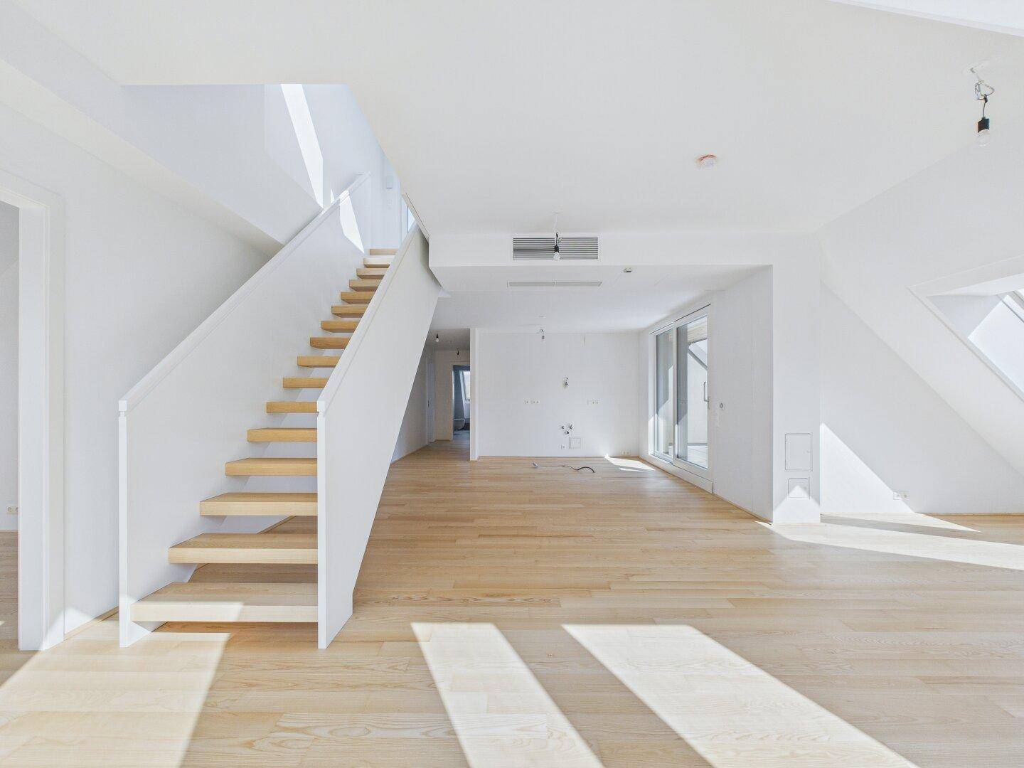 Geräumiges, leeres Wohnzimmer mit hellem Parkettboden und Zugang zu einem Balkon.