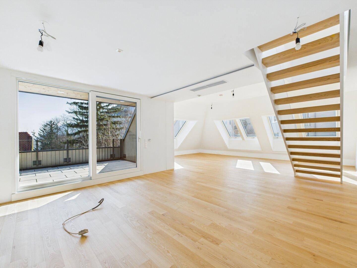 Heller, leerer Raum mit Holzboden, Dachfenstern und Zugang zu einer großen Terrasse.