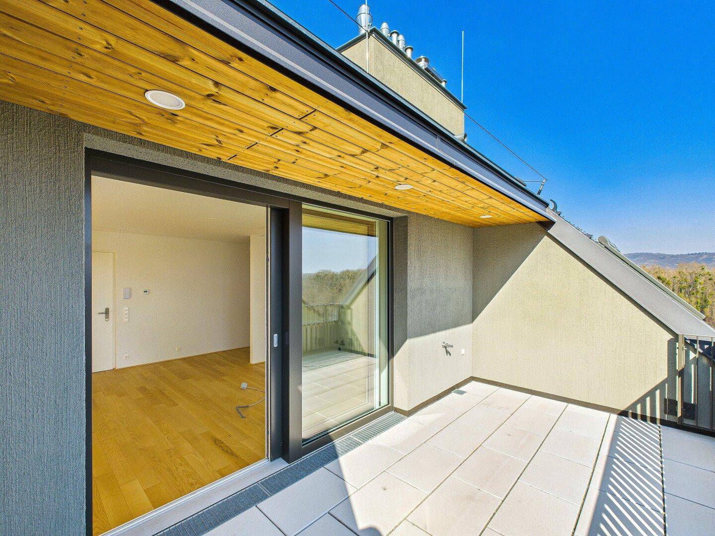 Geräumige Terrasse mit Fliesenboden und Holzdach, direkt zugänglich vom Innenbereich.
