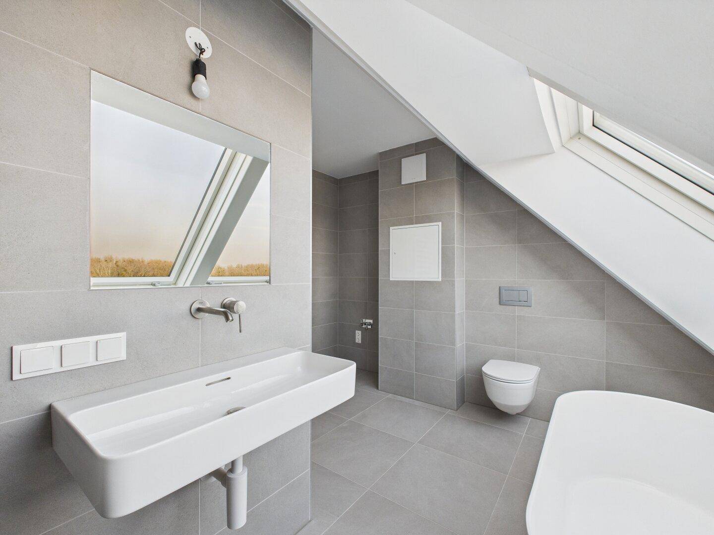Modernes Badezimmer mit großem Waschbecken, Wand-WC und grauen Fliesen im Dachgeschoss.