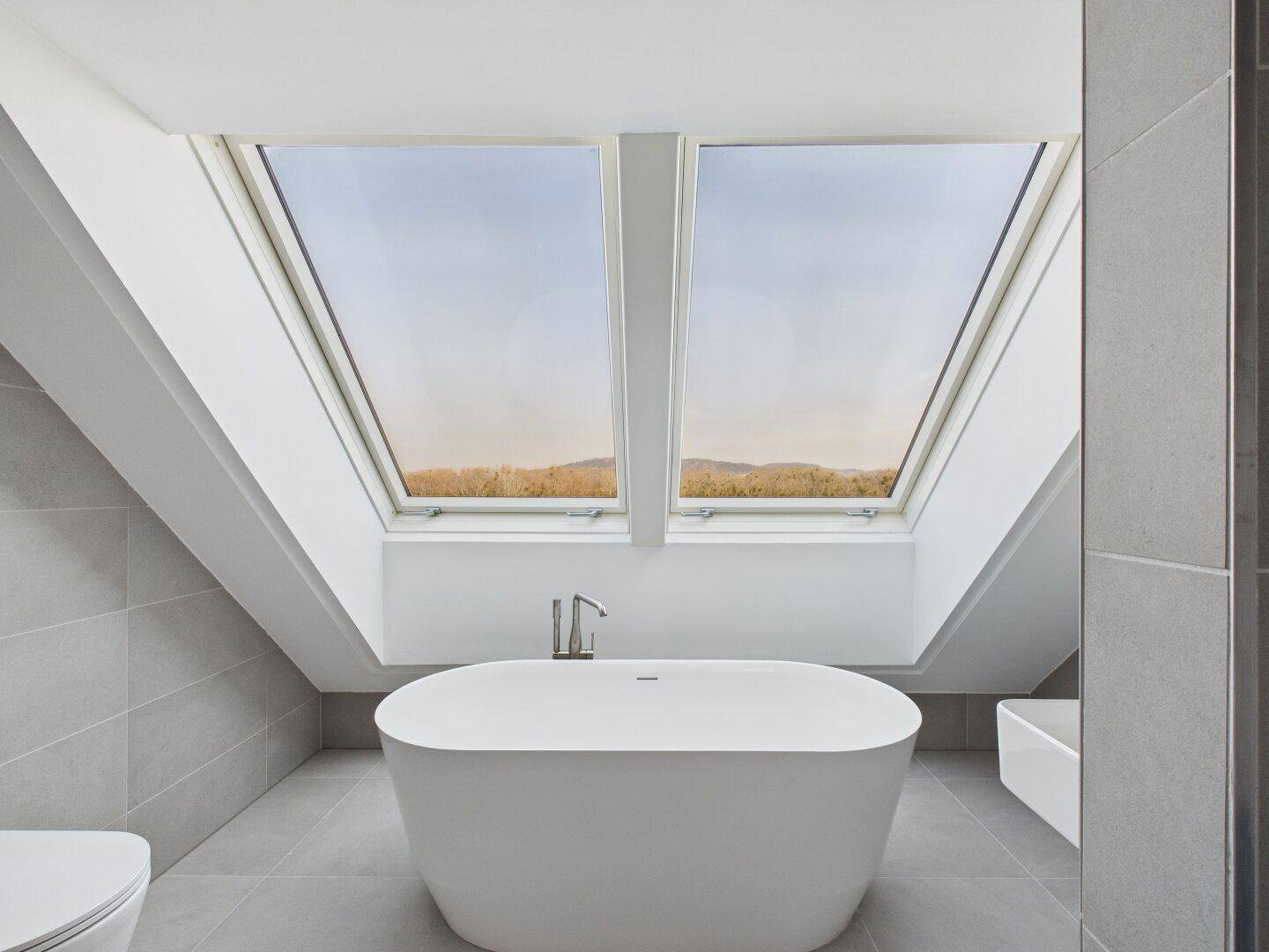 Helles Badezimmer mit freistehender Badewanne und zwei großen Dachfenstern mit Weitblick.