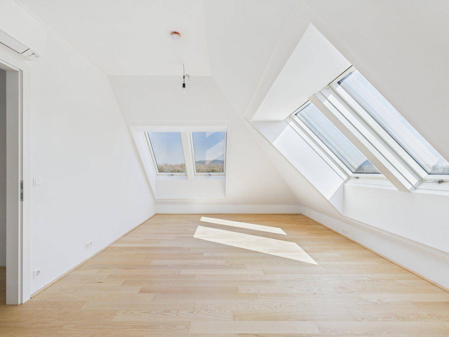 Geräumiges Dachgeschosszimmer mit hellem Holzboden und mehreren Dachfenstern für viel Licht.