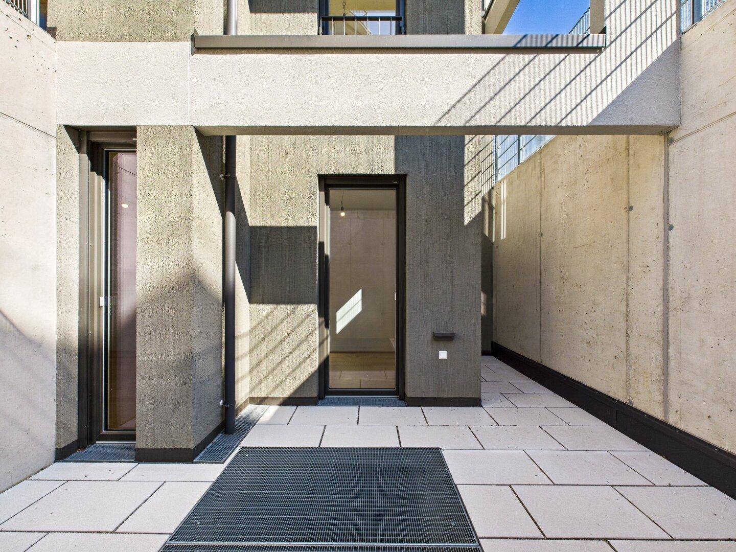Überdachte Terrasse mit modernen Betonwänden und Zugang zum Gebäude, ideal für entspannte Stunden.