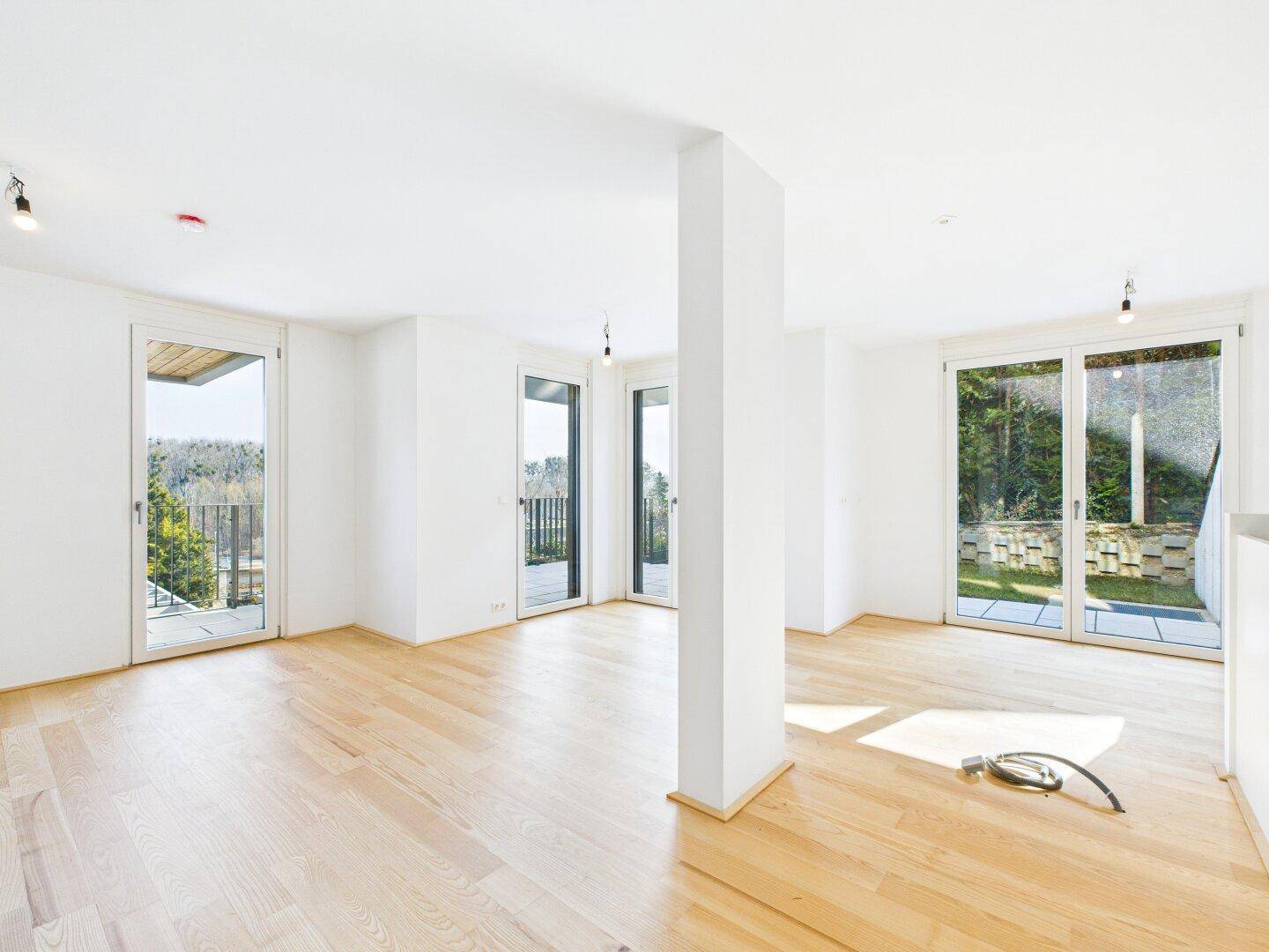 Helles, leeres Wohnzimmer mit Parkettboden und Zugang zu Balkon und Terrasse.