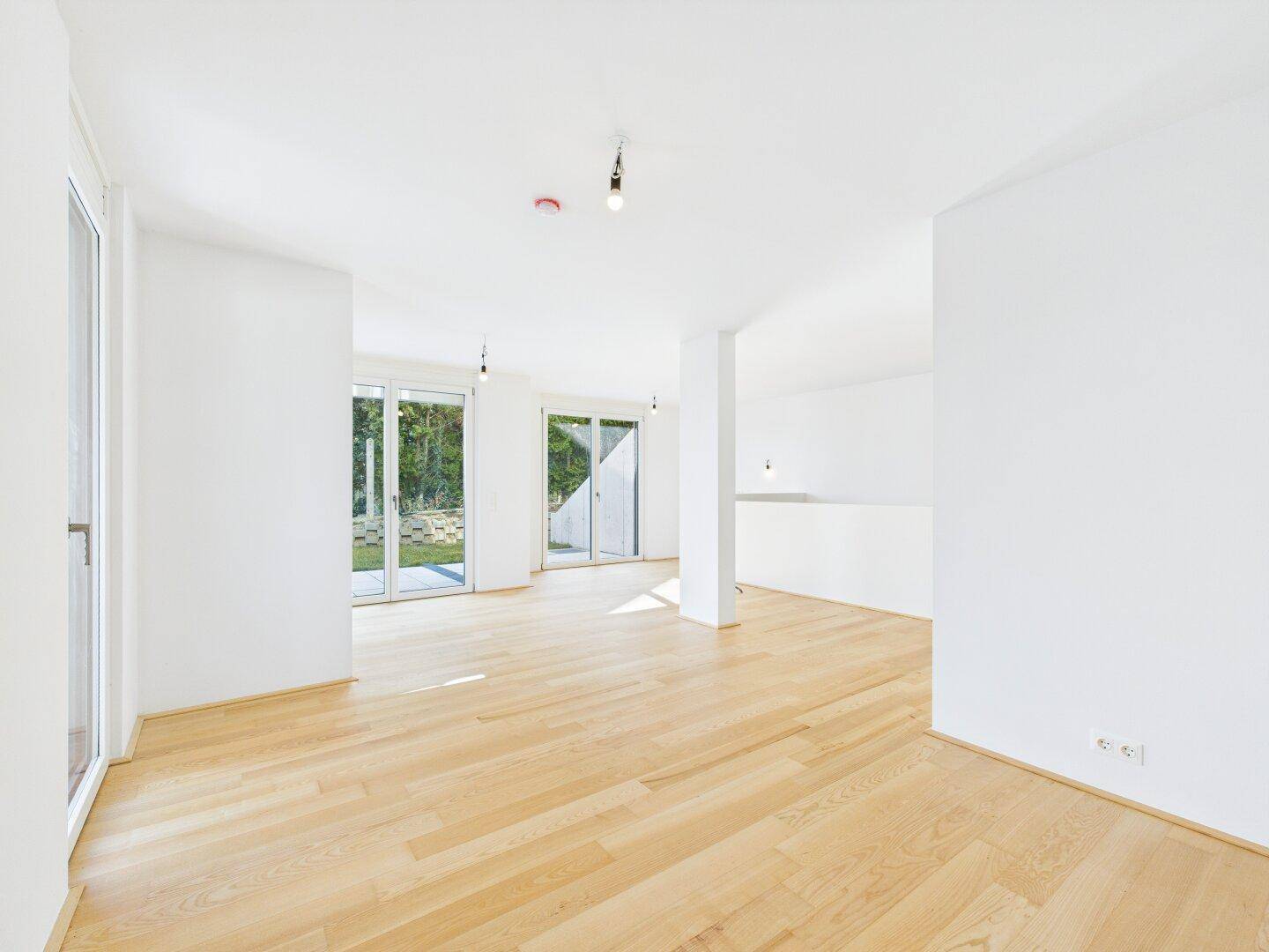 Geräumiges, helles Wohnzimmer mit Holzboden und Blick ins Grüne durch große Fenster.