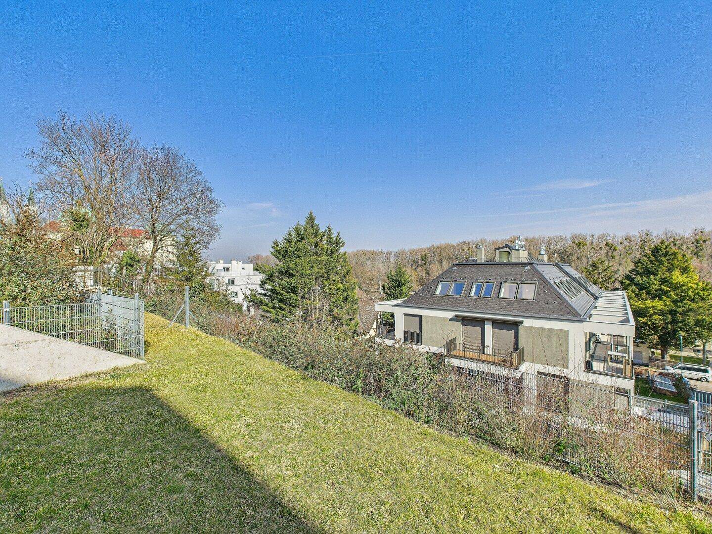 Panoramablick über die grüne Umgebung mit weiteren Gebäuden und Bäumen unter blauem Himmel.
