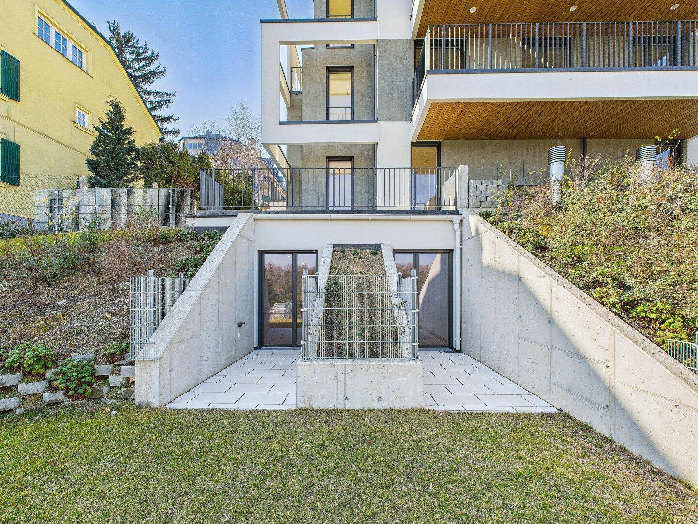 Untere Terrasse mit Betonwänden, gepflastertem Boden und Zugang zu den Innenräumen.
