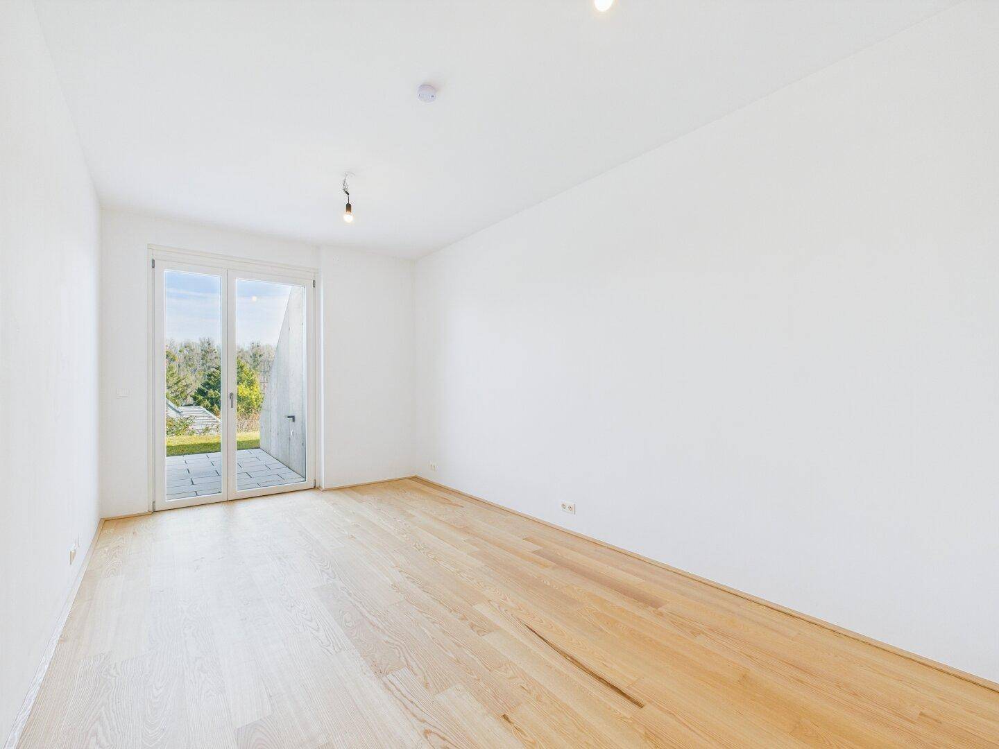 Helles, unmöbliertes Zimmer mit Parkettboden und großem Fenster zum Außenbereich.