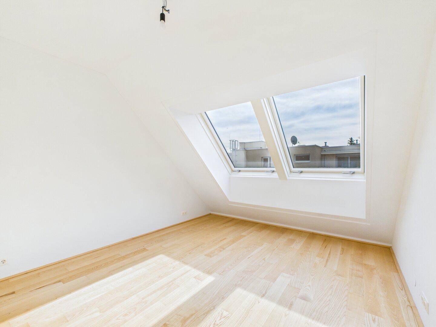 Helles Zimmer im Dachgeschoss mit Holzboden und schrägen Wänden, ideal für ein Schlafzimmer.