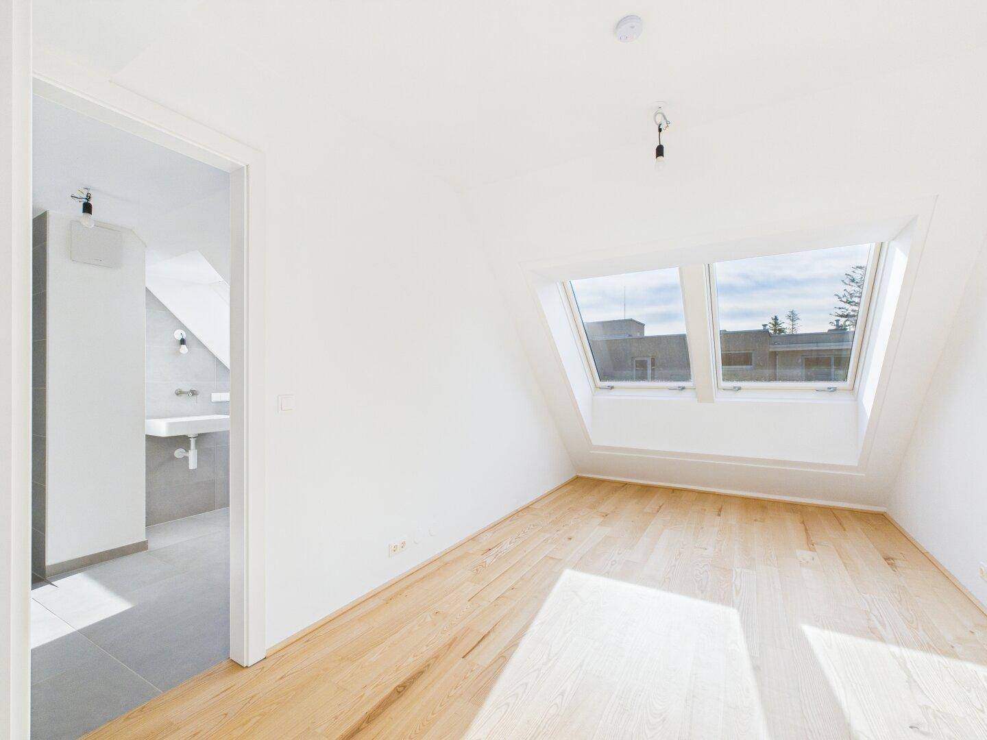 Geräumiges Dachgeschosszimmer mit Holzboden und Zugang zu einem modernen Badezimmer.