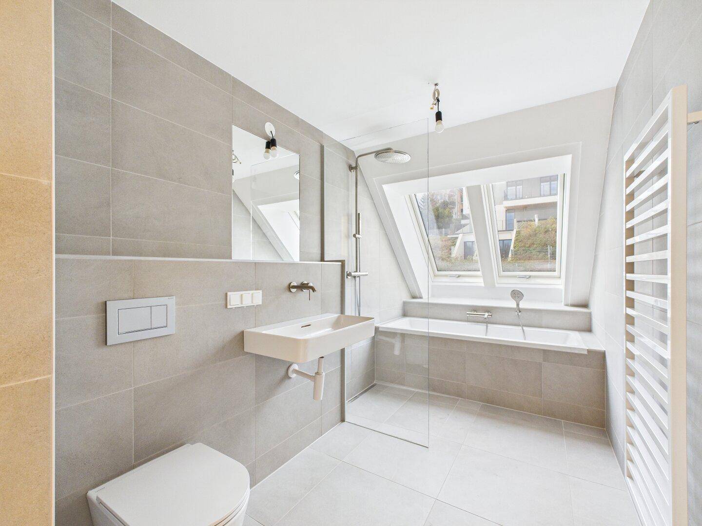 Modernes Badezimmer mit grauen Fliesen, Badewanne, Dusche und Dachfenster.