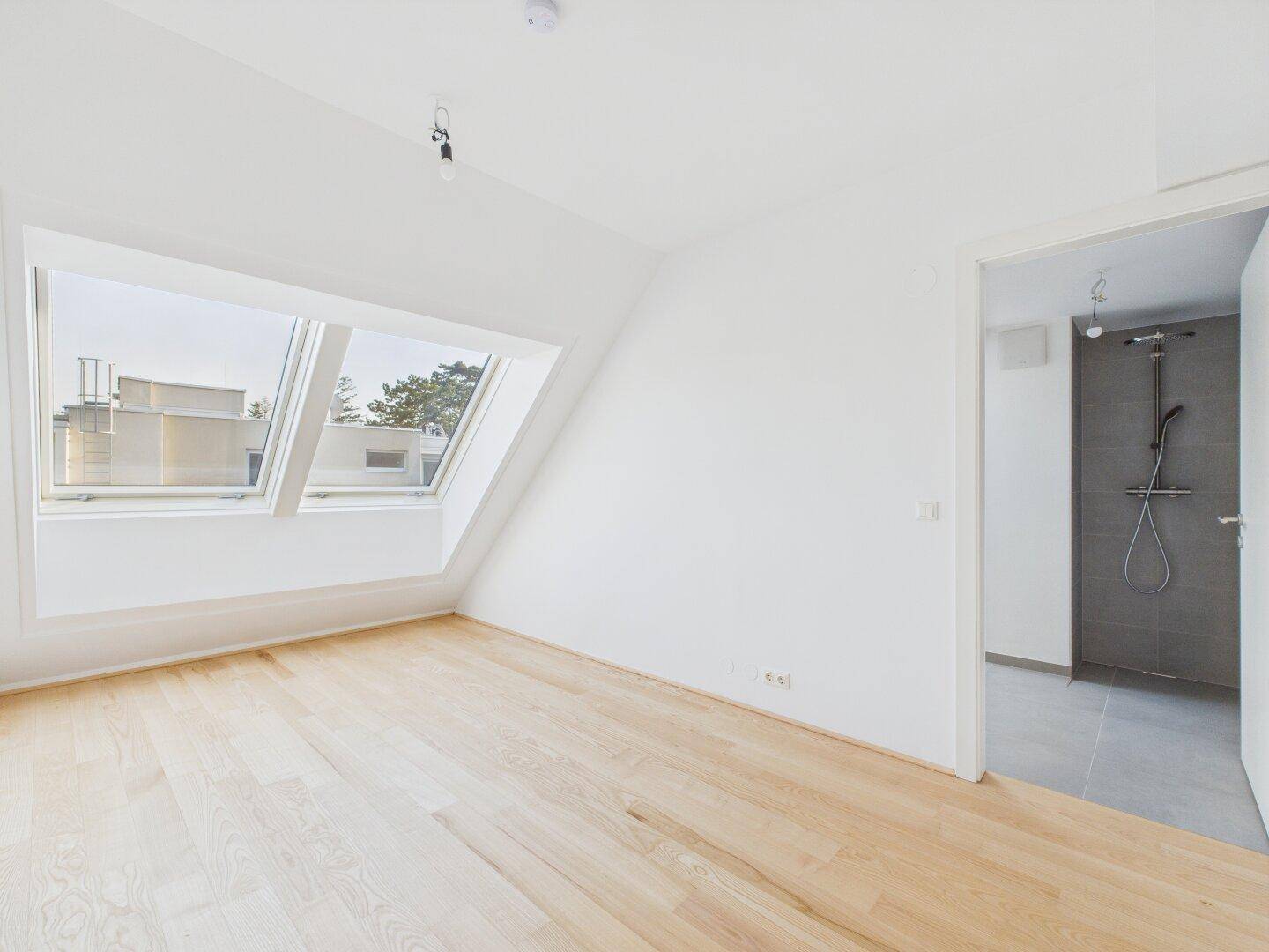 Helles Schlafzimmer im Dachgeschoss mit Holzboden und direktem Zugang zu einem modernen Duschbad.