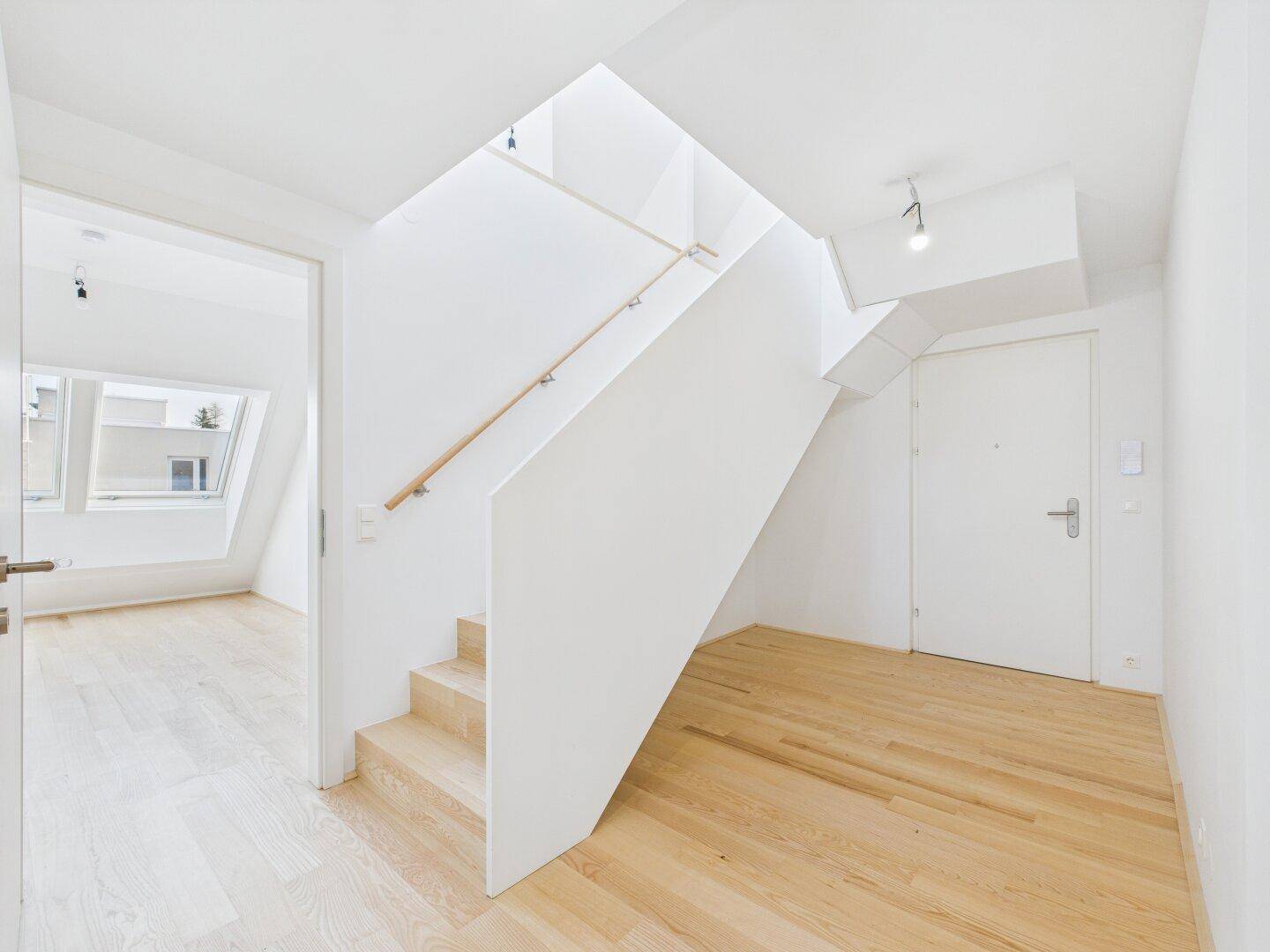 Heller Eingangsbereich mit moderner Treppe und Holzboden, der zu den oberen Etagen führt.