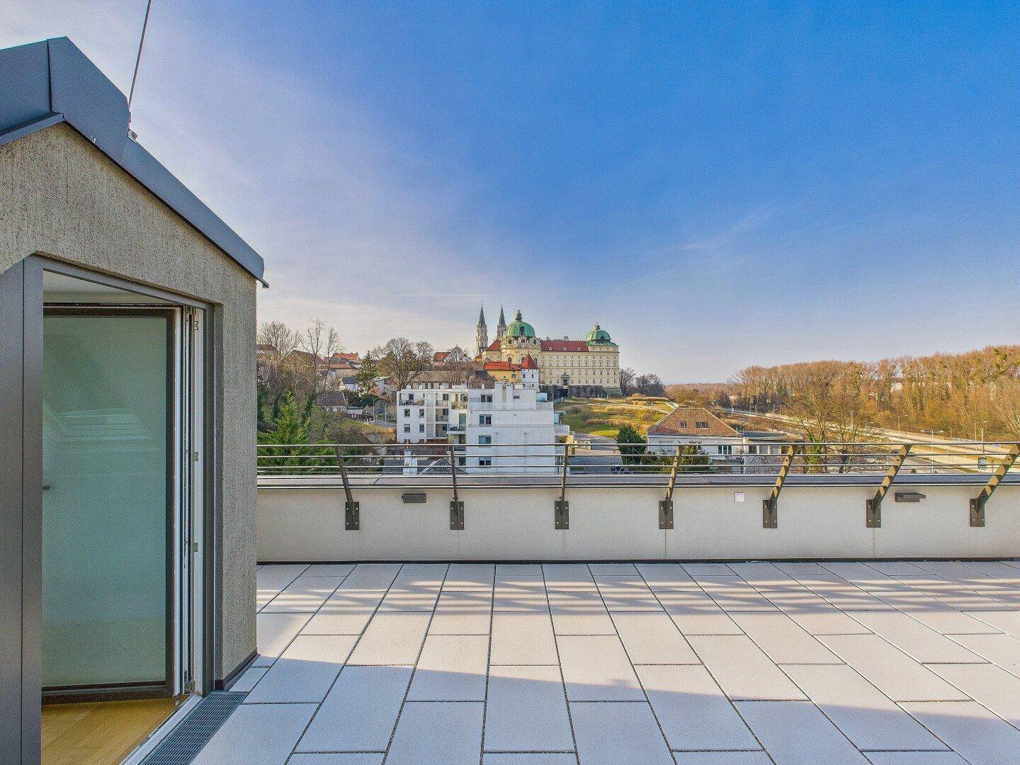 Weitläufige Dachterrasse mit Fliesenboden und Panoramablick auf eine historische Klosteranlage.
