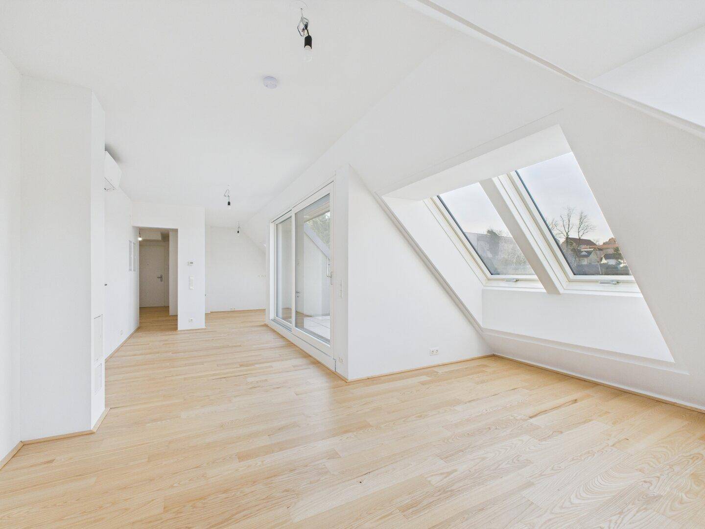 Geräumiges, leeres Wohnzimmer im Dachgeschoss mit hellen Holzböden und großen Dachfenstern.