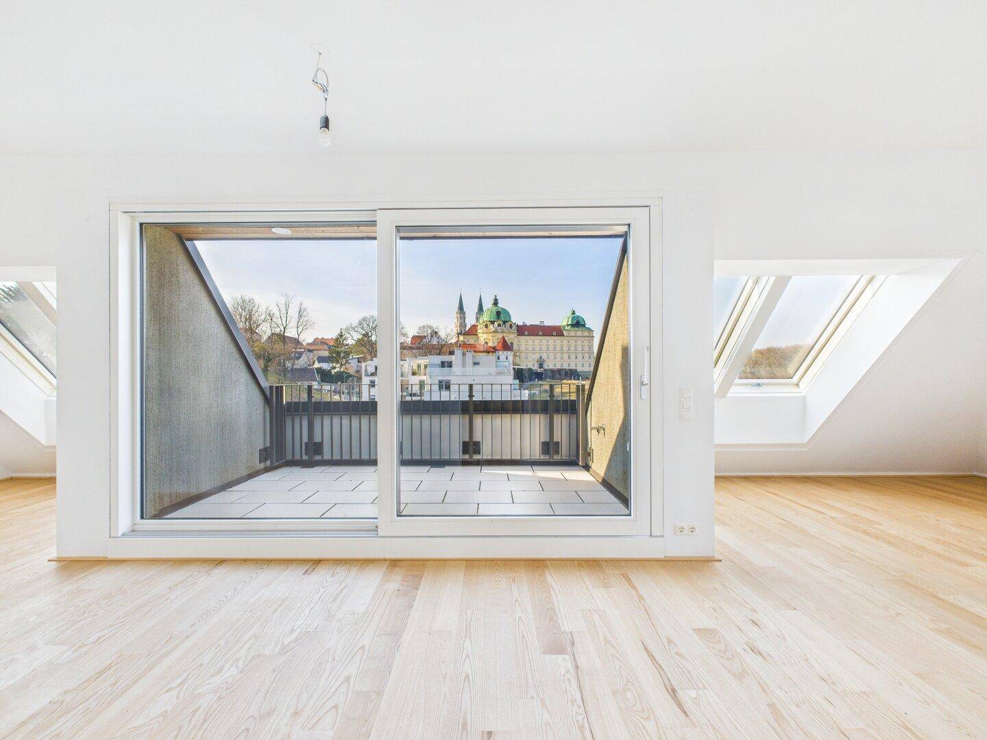Heller Wohnraum im Dachgeschoss mit Holzboden und Zugang zu einer Terrasse mit Stadtblick.