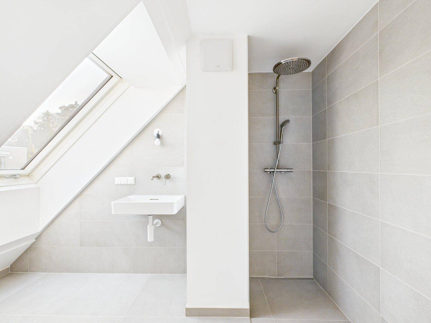 Modernes Badezimmer im Dachgeschoss mit begehbarer Dusche, Waschbecken und Dachfenster.