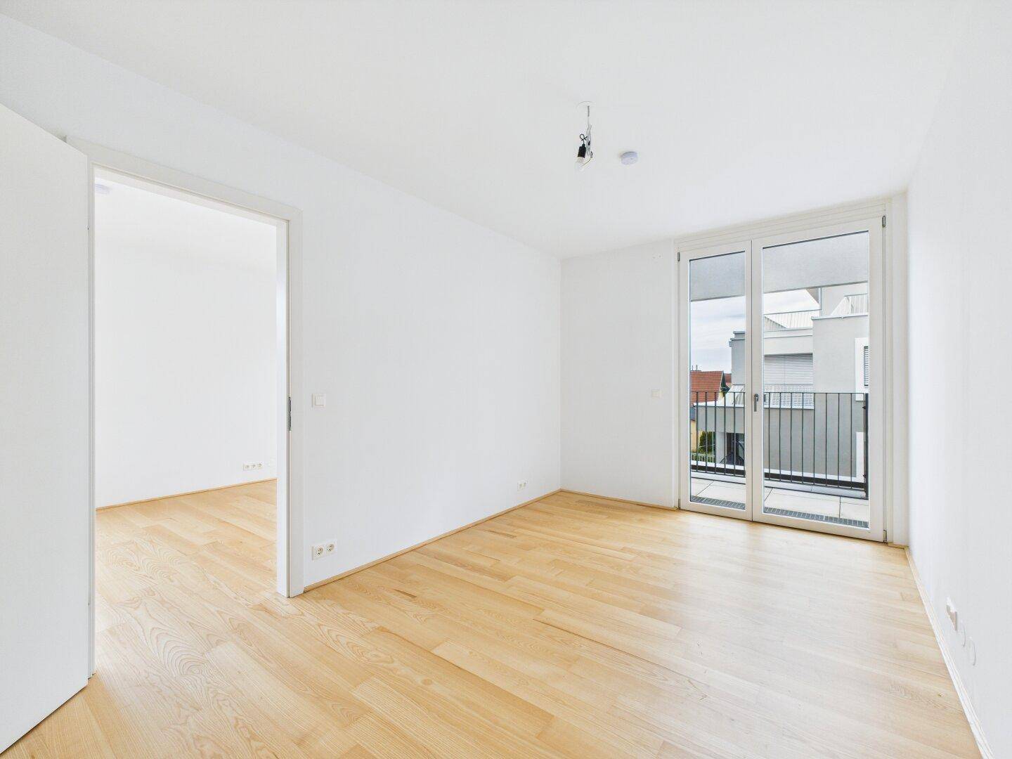 Helles Zimmer mit Parkettboden und Zugang zu einem kleinen Balkon, ideal als Schlaf- oder Arbeitszimmer.
