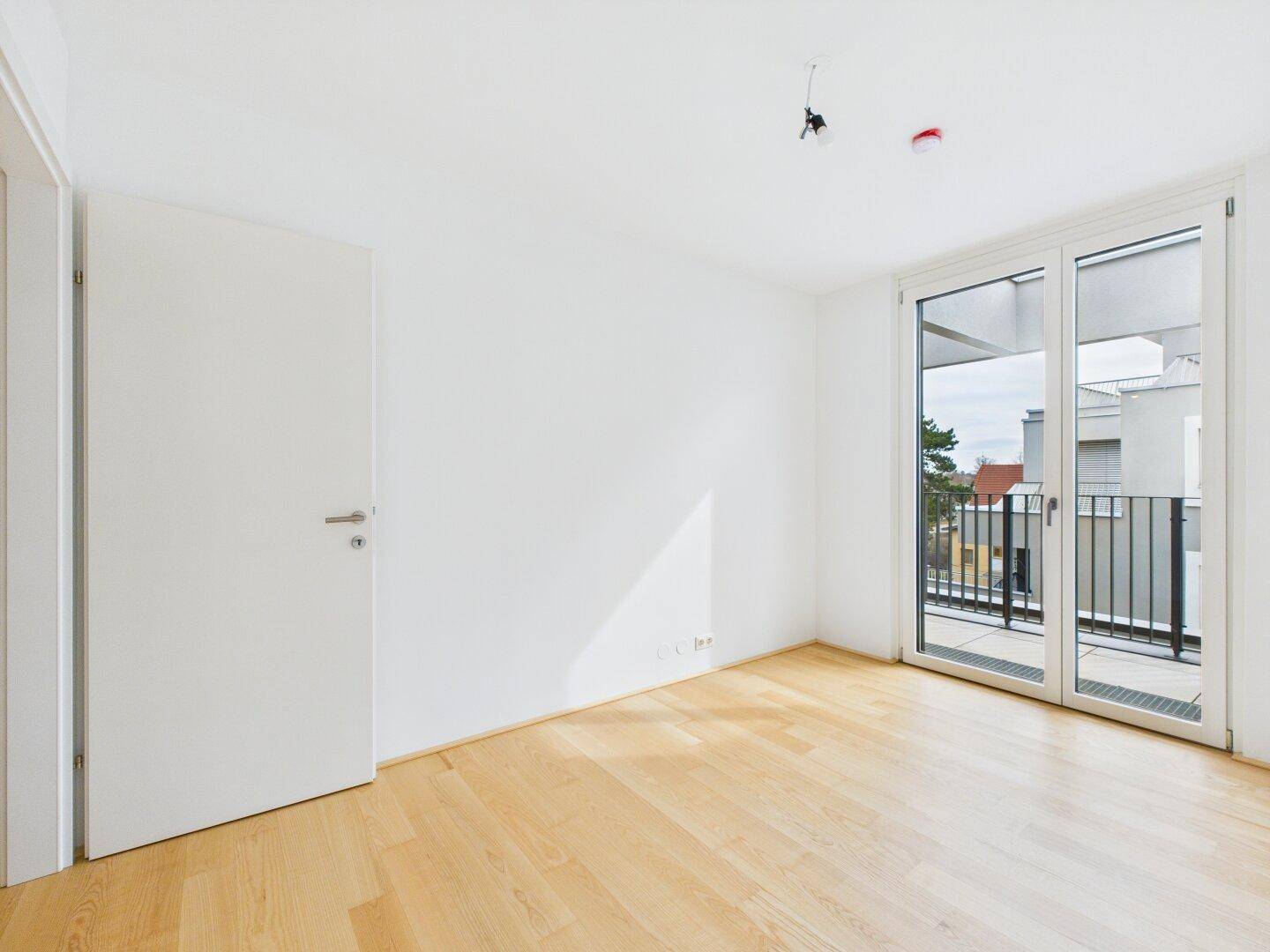 Lichtdurchflutetes Zimmer mit Holzboden und Balkontür, bereit für individuelle Gestaltung.