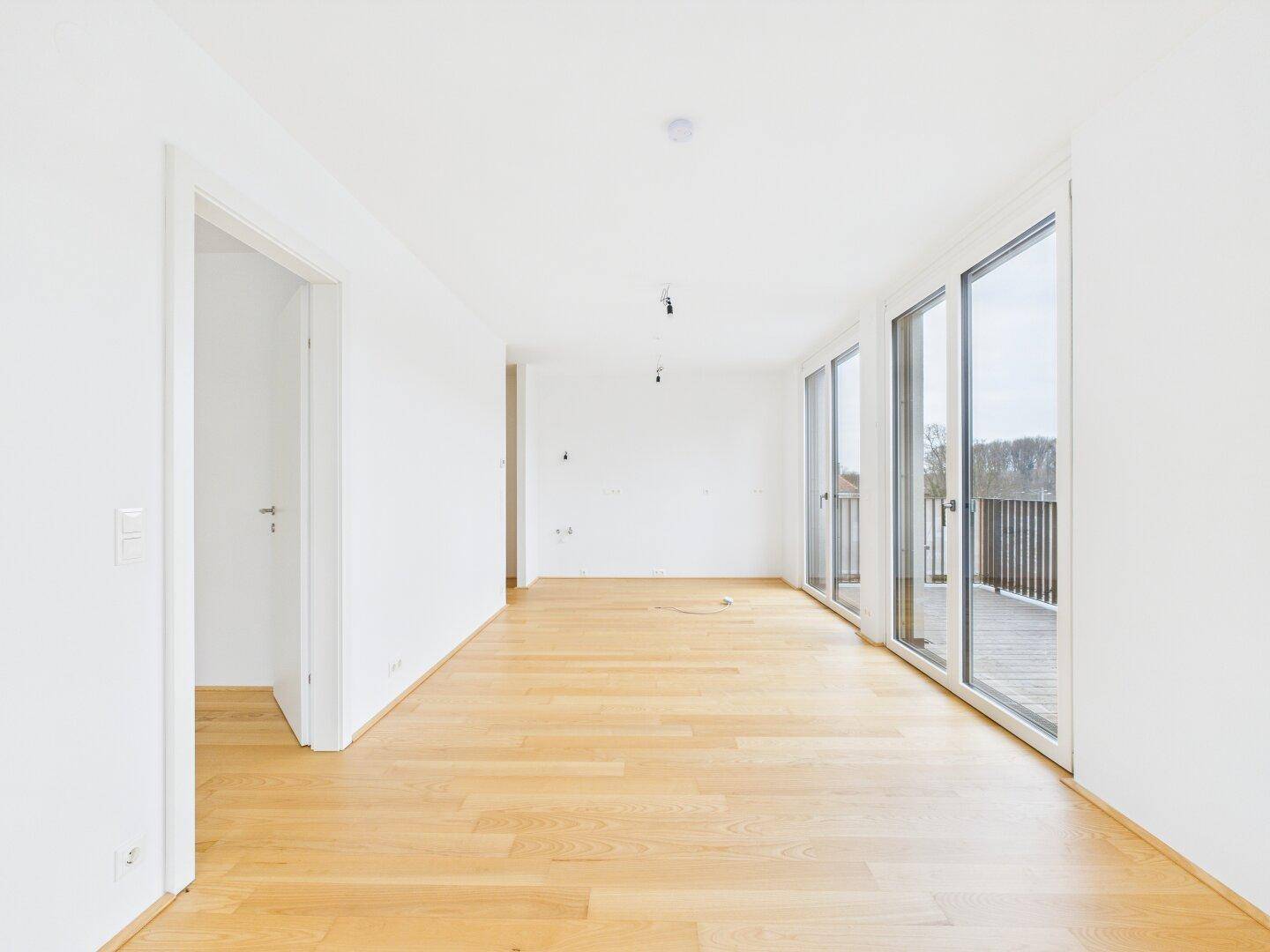 Geräumiger, heller Innenraum mit Holzboden und großen Fenstern, die viel Tageslicht hereinlassen.