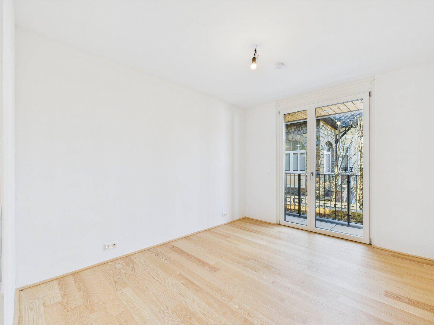 Helles Zimmer mit Holzboden und Zugang zu einem französischen Balkon, ideal als Schlafzimmer.