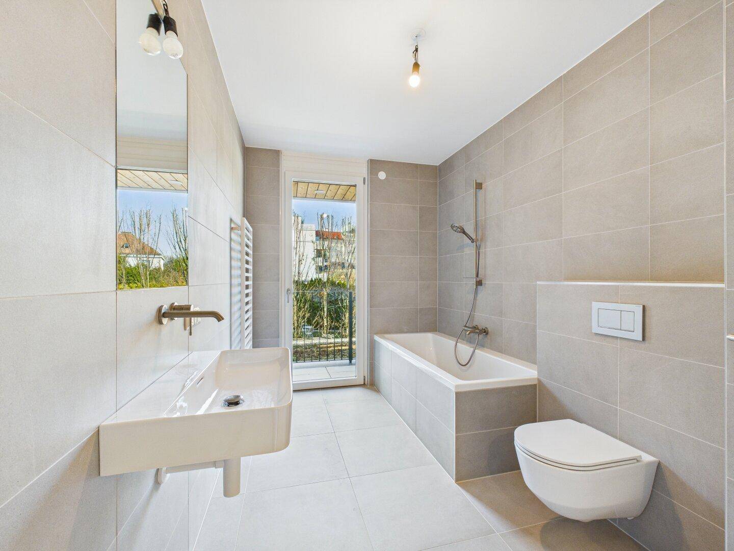 Modernes Badezimmer mit hellgrauen Fliesen, Badewanne und Waschtisch, bietet direkten Zugang nach draußen.