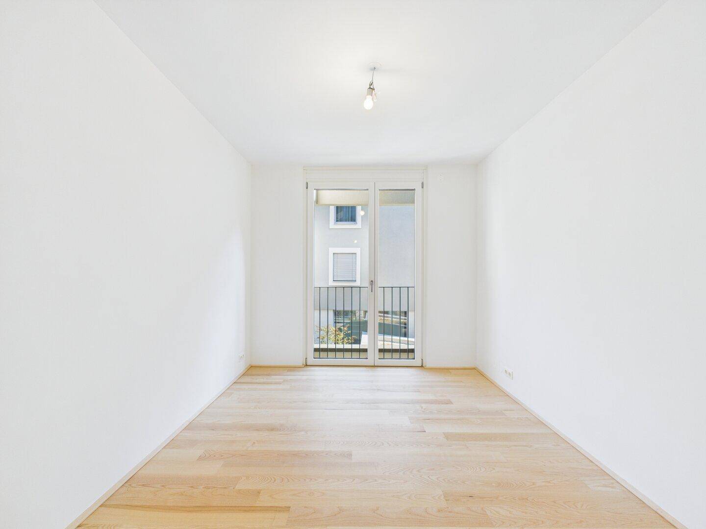 Leeres, helles Zimmer mit Parkettboden und Zugang zu einem kleinen Balkon, ideal für individuelle Gestaltung.